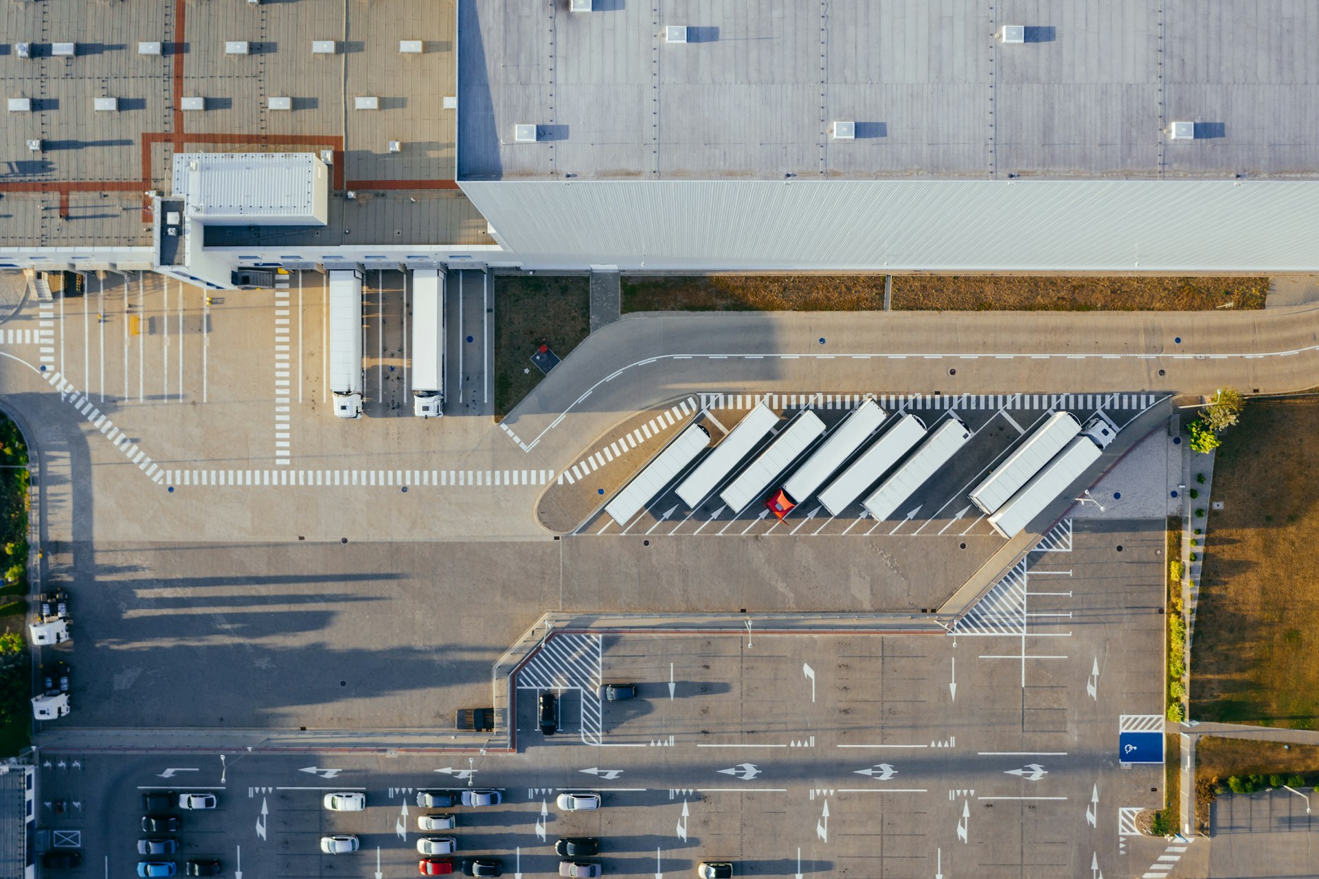 A distribution centre seen from directly above, with white trailers angled into their bays and lorries at the loading docks