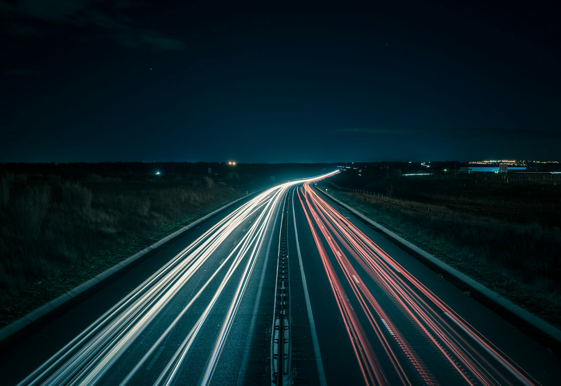 A motorway at night, with the light trails of headlights and tail lights drawn out along both carriageways