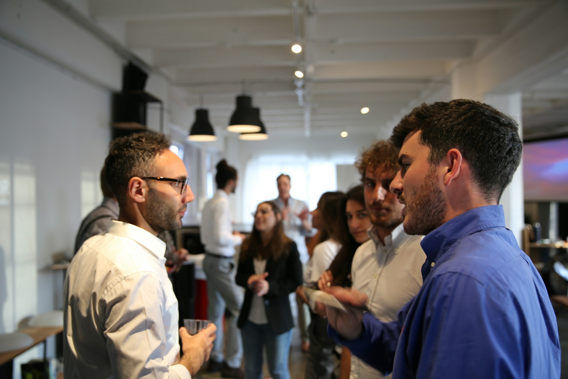 Professionals standing in conversation in small groups in a bright, open office