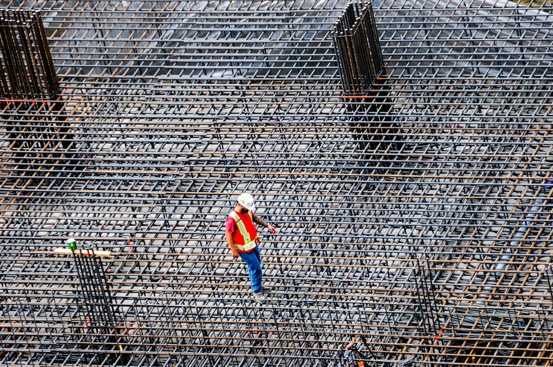A worker in a white hard hat and orange hi-vis vest standing on a reinforcing-steel deck that fills the frame