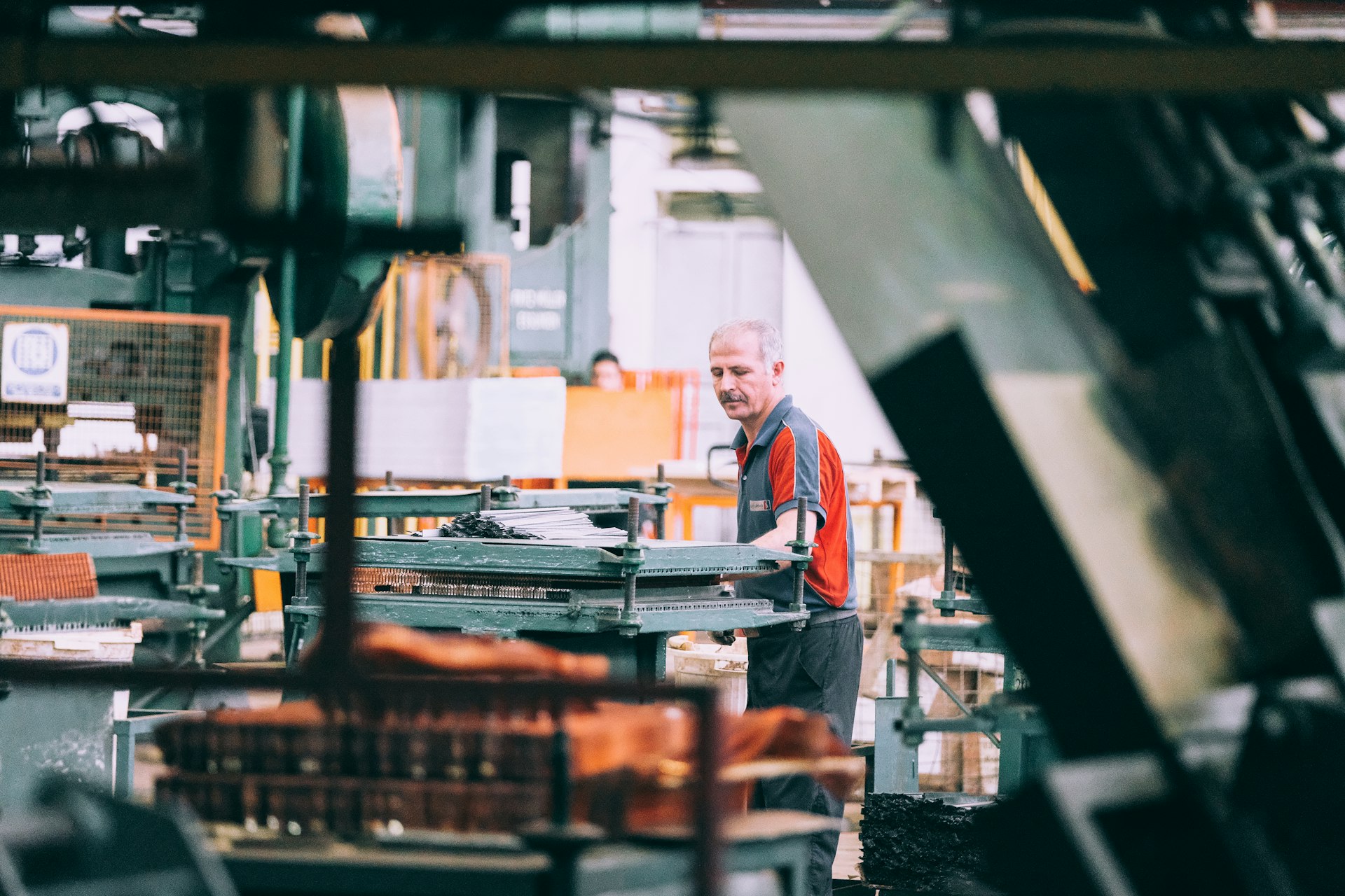 A machine operator working at a press in a metalworking shop, stacked sheet material on the bed