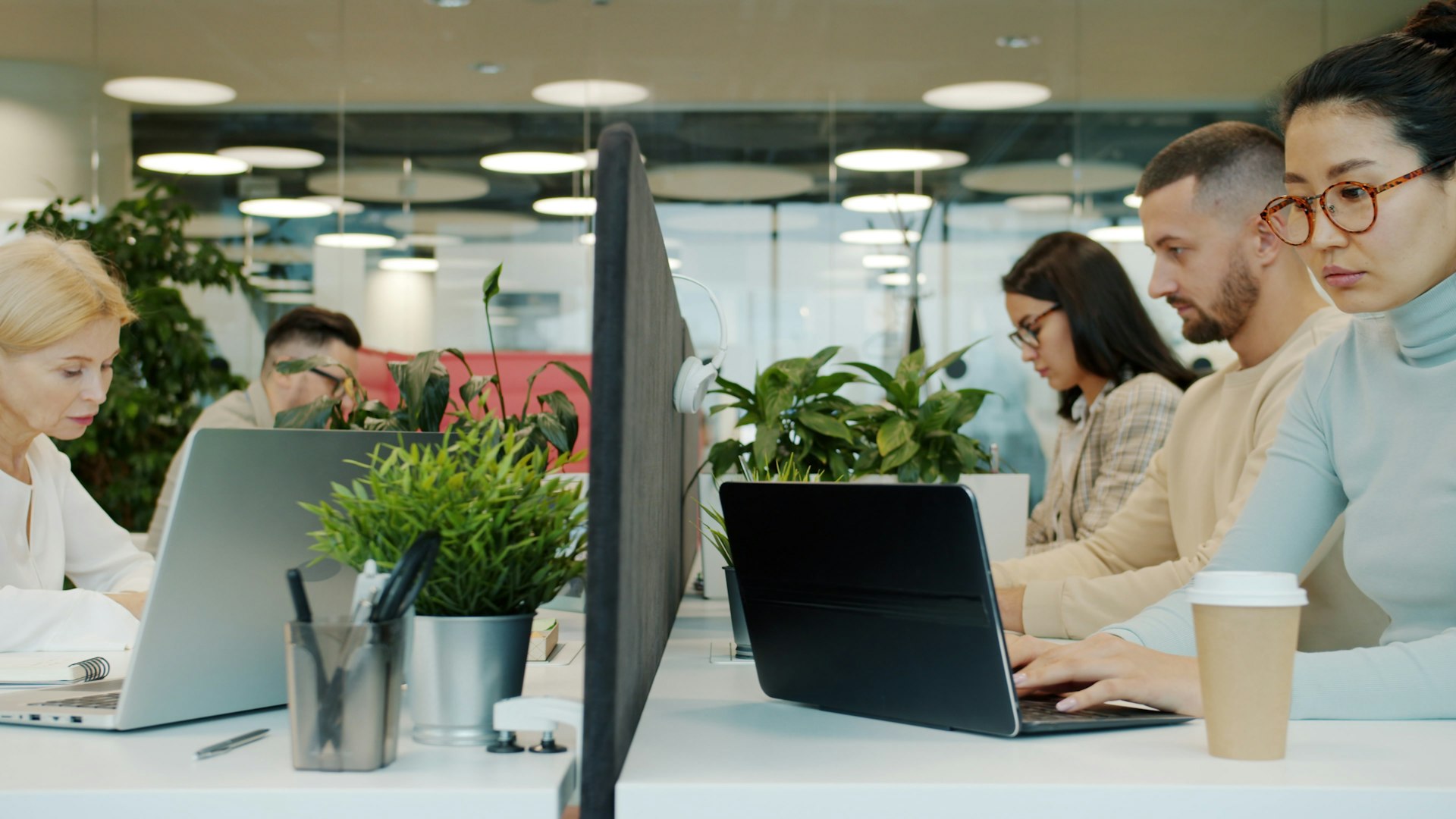 People working at laptops along a long white desk in a bright open-plan office